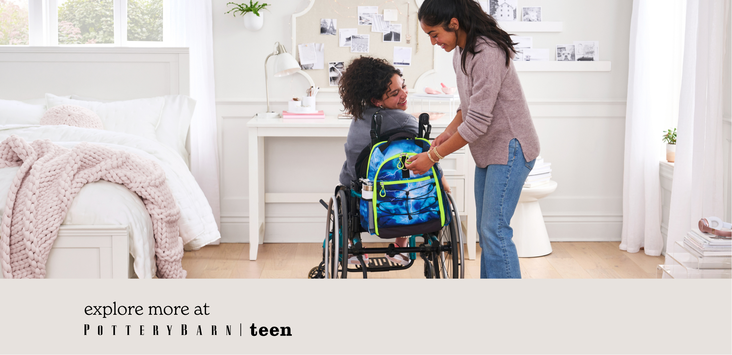 Image shows two teen girls in a white and pink teen girl bedroom. One girl sits in a wheelchair with a Pottery Barn Teen Gear-Up Adaptive Backpack in Storm print attached to it. The other girl stands next to her and helps to unzip the backpack.