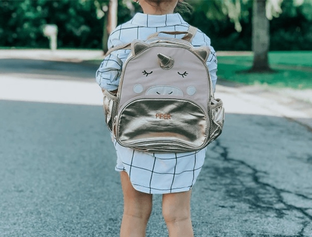 Young child standing in street wearing a unicorn backpack.