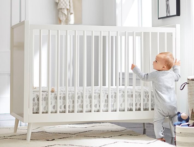 baby standing next to white crib