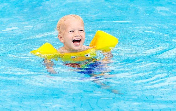 Happy infant playing in water with arm floaties