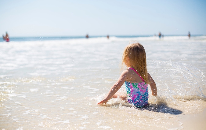 Young girl in magenta and blue swimsuit playing in the ocean 