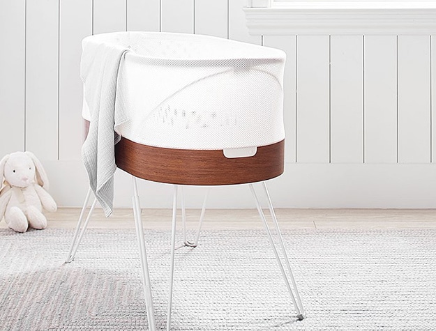 A stylish bassinet sitting in the middle of a sunlit room on a white rug.
