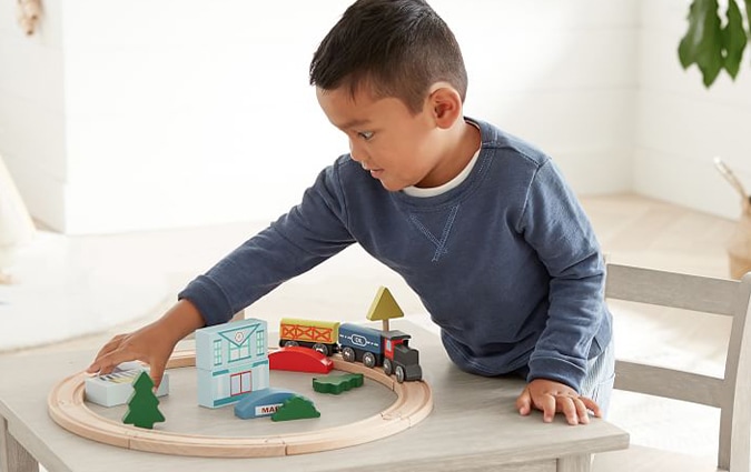 Young boy playing with wooden train set on table