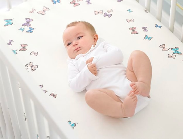 Baby on butterfly sheets in crib.