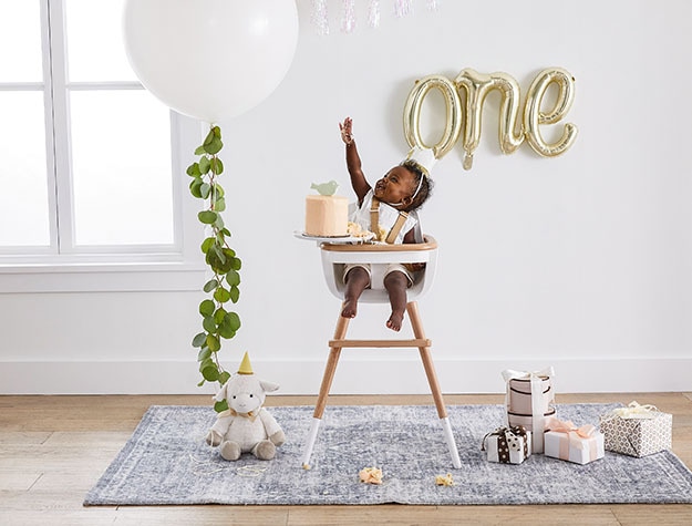 Baby in high chair with balloons spelling one
