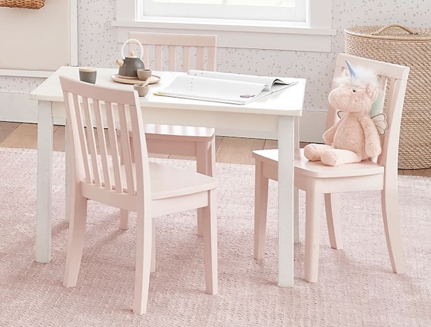 Unicorn plush toy sitting on a light pink chair at a small white table