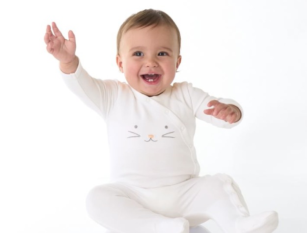  smiling baby sitting on floor wearing white onesie with bunny face print