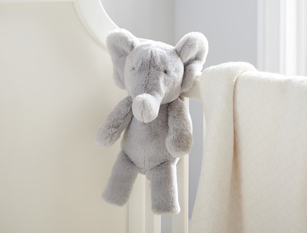 plush elephant suspended from side of crib next to a blanket