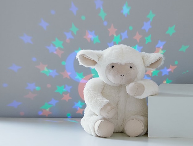 plush lamb nightlight emitting colorful light display on wall behind it