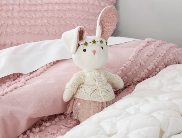 dressed rabbit doll with floral headband on pink and white bed