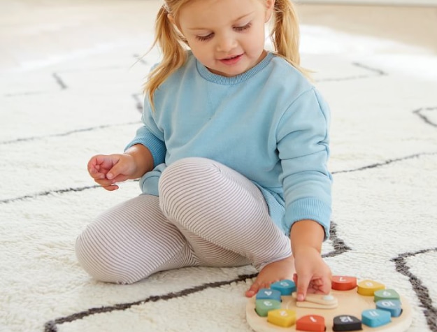 young girl wearing blue sweater plays with colorful wooden clock toy