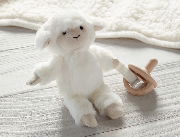 Plush lamb toy holding a pacifier on bed