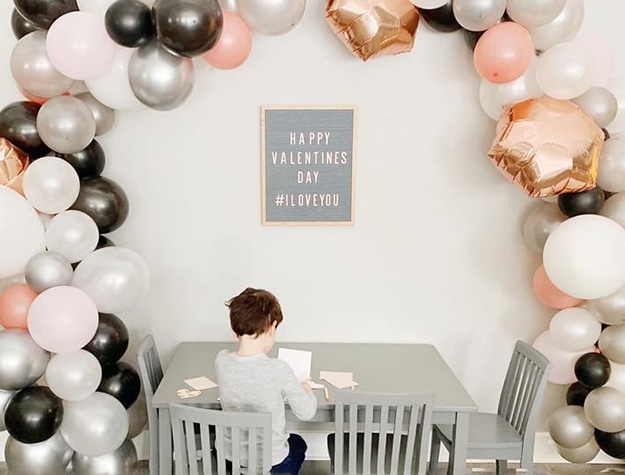 Large play table with balloons and kid seated at table.