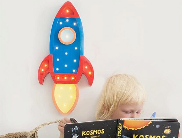 Kid reading book with a Little Lights Rocket Lamp hanging behind them. 