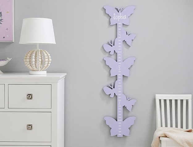 Butterfly shaped growth hanging chart near white dresser and lamp.