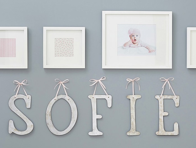 Monique lhuillier ribbon letters hanging beneath white framed images against gray wall.