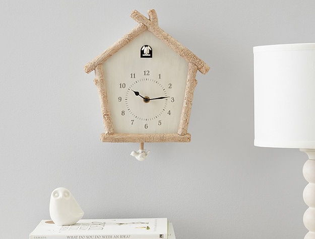 Birch cuckoo clock on wall above white bird figurine sitting on books with lamp on the side. 