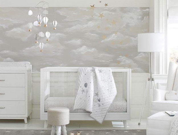 Clouds wallpaper in nursery behind white crib with white rocker on the side and changing table.