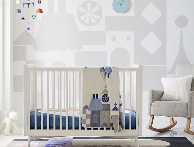 Shape pattern wallpaper with hanging mobile above white crib and rocker. 