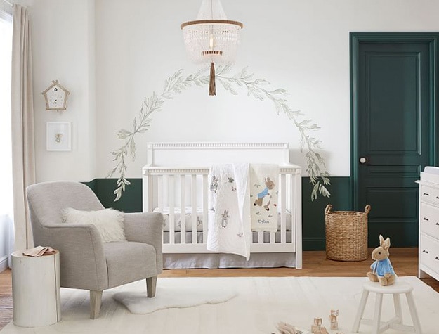 Foliage arch above crib and gray seat to the side and stool with bunny toy. 