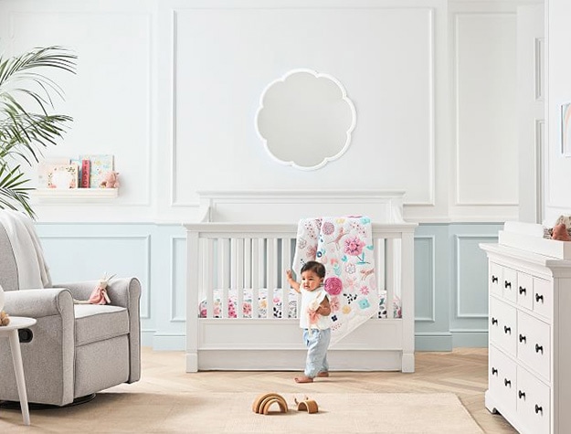 Larkin 4-in-1 convertible crib with baby in front, mirror above and rocker to the side. 