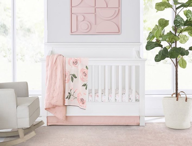 Larkin convertible crib with pink wall art above and pink blanket hanging over.