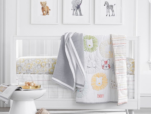 Animal themed nursery with lion blanket on white crib against wall with framed animal prints.