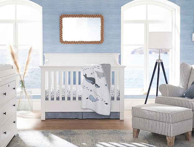 Blue tone nursery wallpaper with white crib and stripe rocker with ottoman. 