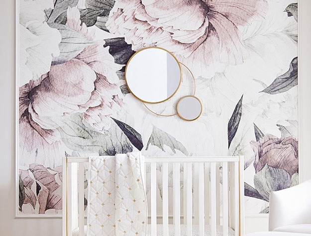 Floral wallpaper with gold mirror and white crib.