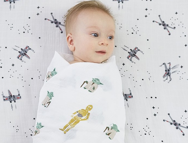 Baby wrapped in Star Wars themed baby swaddle on top of themed crib sheets.