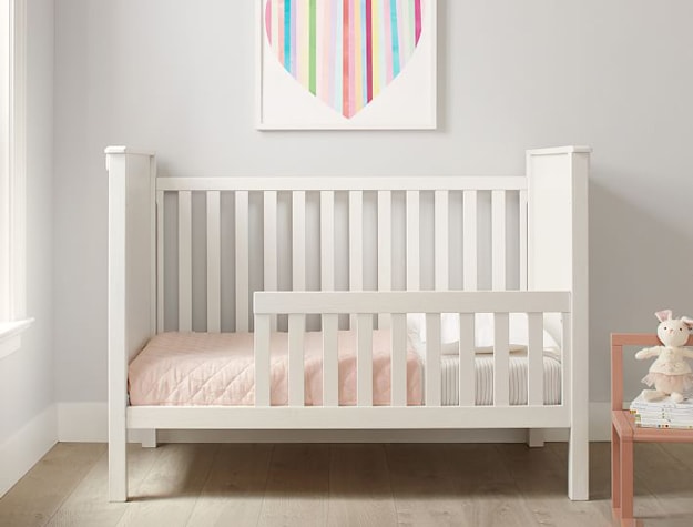 White Rory Convertible Crib in girl’s room with pink blanket.