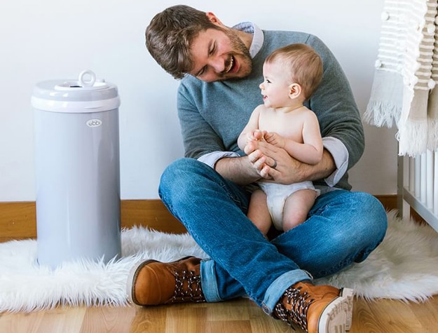 Dad and baby sitting on floor next to gray Ubbi Diaper Pail.