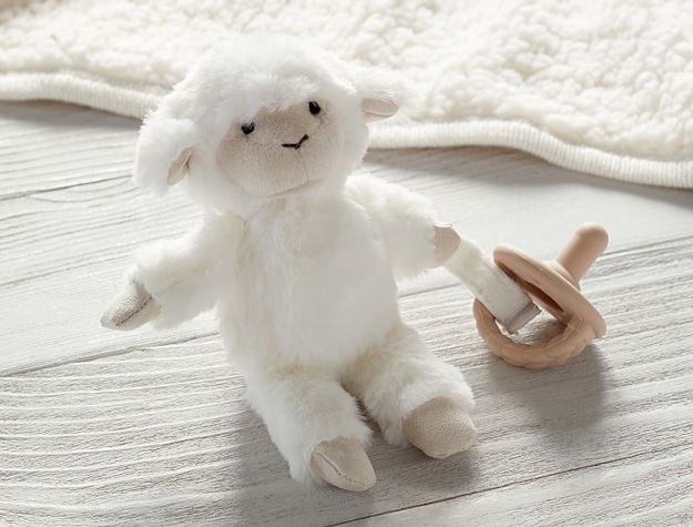 Lamb Critter Plush Pacifier Holder with pacifier on a wooden table.