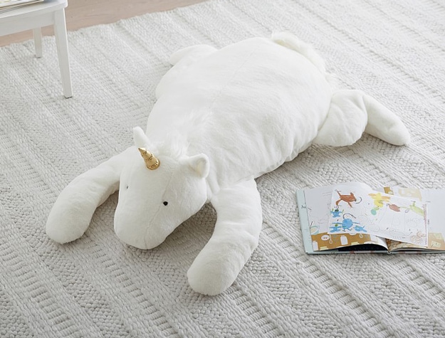Unicorn Jump Floor Plush on a white rug next to an open children’s book.