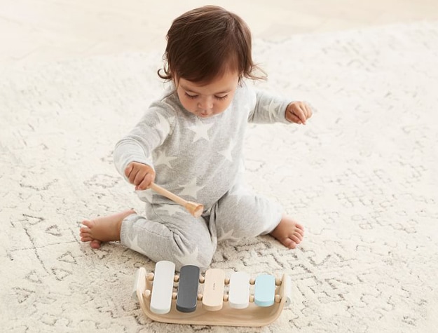 Child playing with a Plan Toys xylophone on the floor.