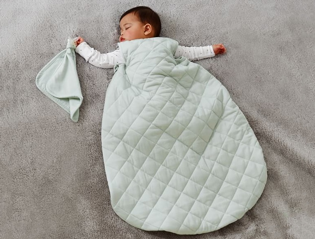 Baby sleeping on a gray quilt wearing a Green TENCEL™ Jersey Adjustable Wearable Blanket.