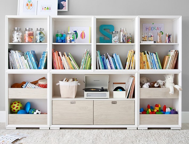 White storage shelves with drawers filled with colorful books and toys.