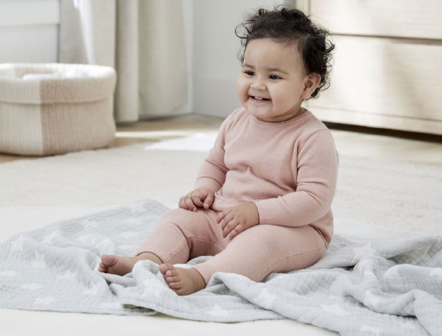 An older baby sits on top of Shining Star Organic Matelassé Baby Blanket during playtime on the floor.