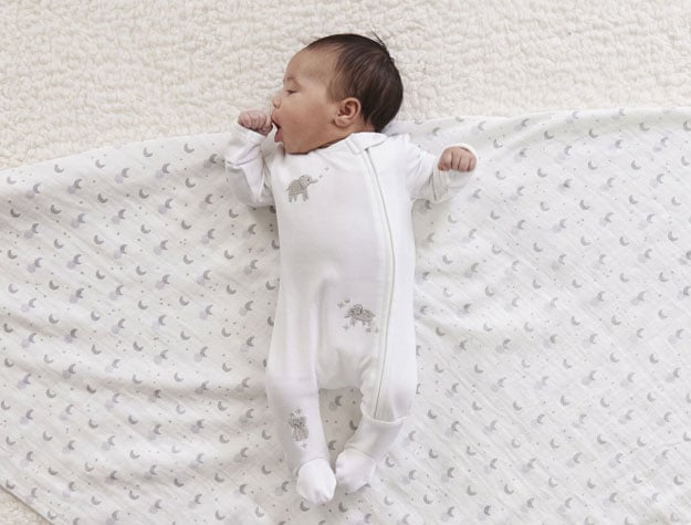 Newborn baby lying on their back on top of a folded receiving blanket from the Skye Organic Swaddle Set.