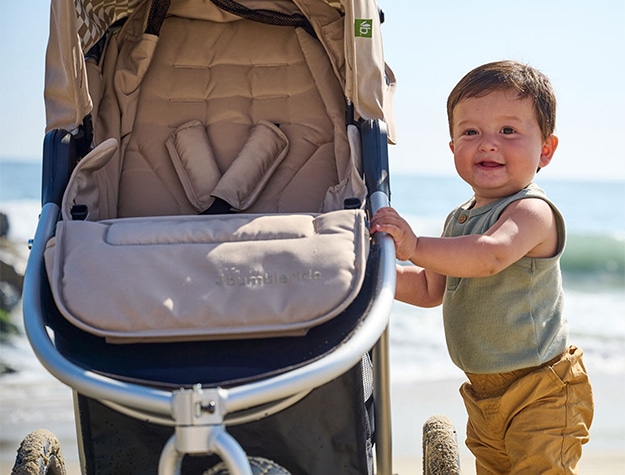 A toddler playing on the beach, holding onto the Bumbleride Indie All-Terrain Stroller.