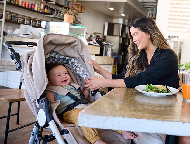 A woman enjoying lunch with a smiling baby seated in the Bumbleride Indie All-Terrain Stroller.