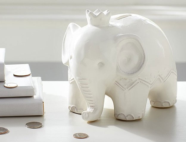 A white elephant piggy bank wearing a crown with coins scattered on the tabletop.