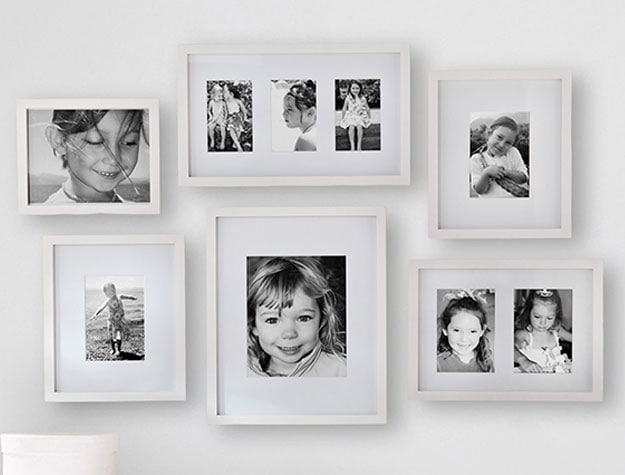Several black and white family photos framed in white frames hung on a mint green wall.