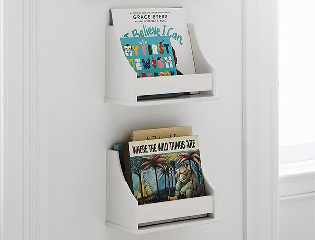 Small bookshelves hung on a white wall with assorted children’s books tucked neatly in place.