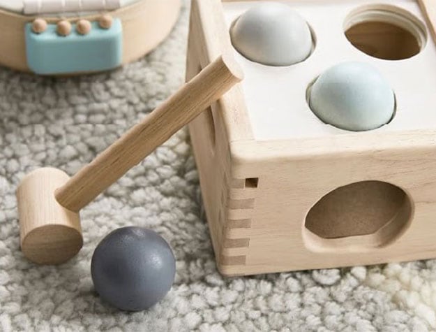 Wooden toys and a mallet rest on a neutral rug.
