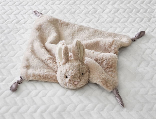 Light tan fuzzy blanket resembling a bunny sitting on a white chevron sheet.