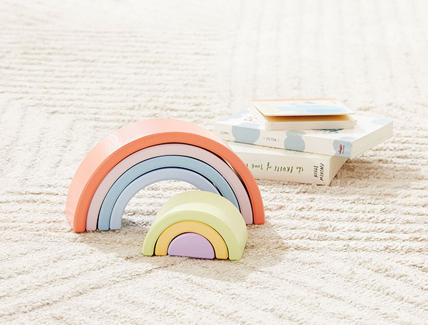 Rainbow stacking toy sitting next to three books on a light cream carpet.