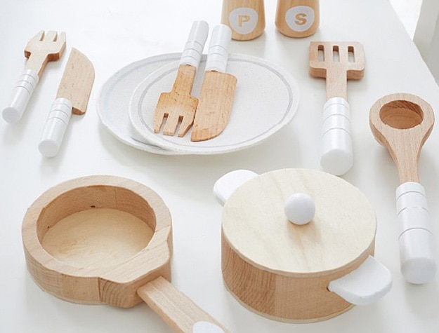 Natural wood and white play kitchen utensils placed on a white table.