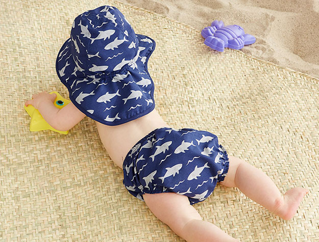Baby wearing a diaper cover and sun hat decorated with sharks.