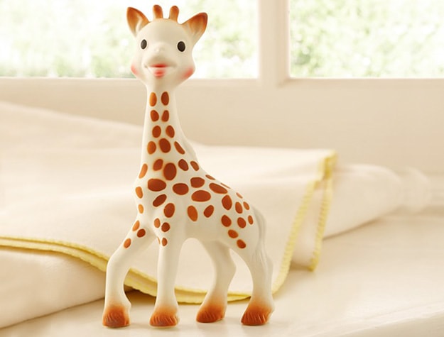Rubber giraffe teether with blankets behind it.